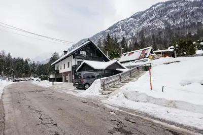 a snow covered street next to a building with a car parked at Mojstranka in Mojstrana