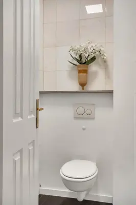 a white bathroom with a toilet and a vase of flowers at Ljubljana Palace Suites in Ljubljana