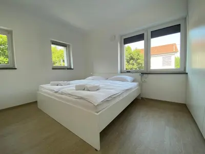 a white bedroom with a large bed with two windows at VILA ADA - 4 Cosy Apartments in Ljubljana