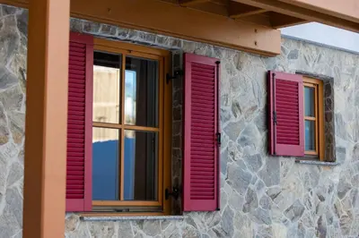 two windows with red shutters on a stone building at Bolfenk Snowflake app in Pohorje