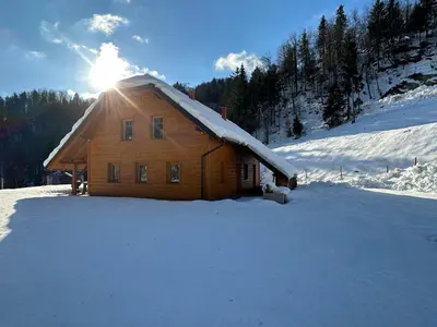 a wooden cabin in the snow with the sun behind it at Chalet HerMes arT in Idrija