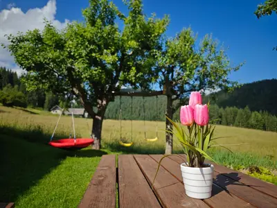 a wooden table with pink flowers and a red swing at Cottage Zoja in Bohinjska Bistrica