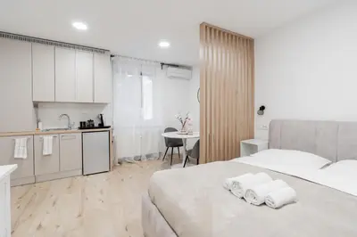 a white bedroom with a large bed and a kitchen at Classy & Cozy apartment in Ljubljana