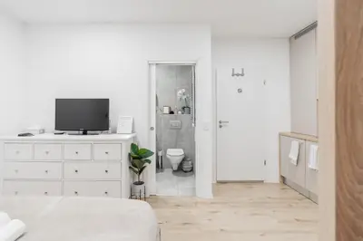 a white bedroom with a television and a bathroom at Classy & Cozy apartment in Ljubljana