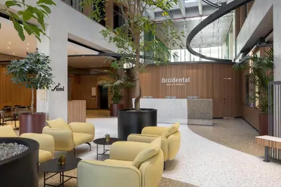 a lobby with yellow chairs and a tree in the center at Occidental Ljubljana in Ljubljana