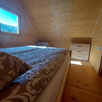 a large bed in a wooden room with a window at Brunarica Jeršin in Cerkno