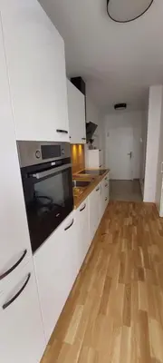 a kitchen with white cabinets and a wooden floor at LA Studio in Maribor