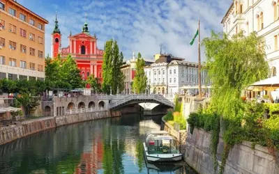 a river in a city with a bridge and a boat at Center Station ROOMS in Ljubljana